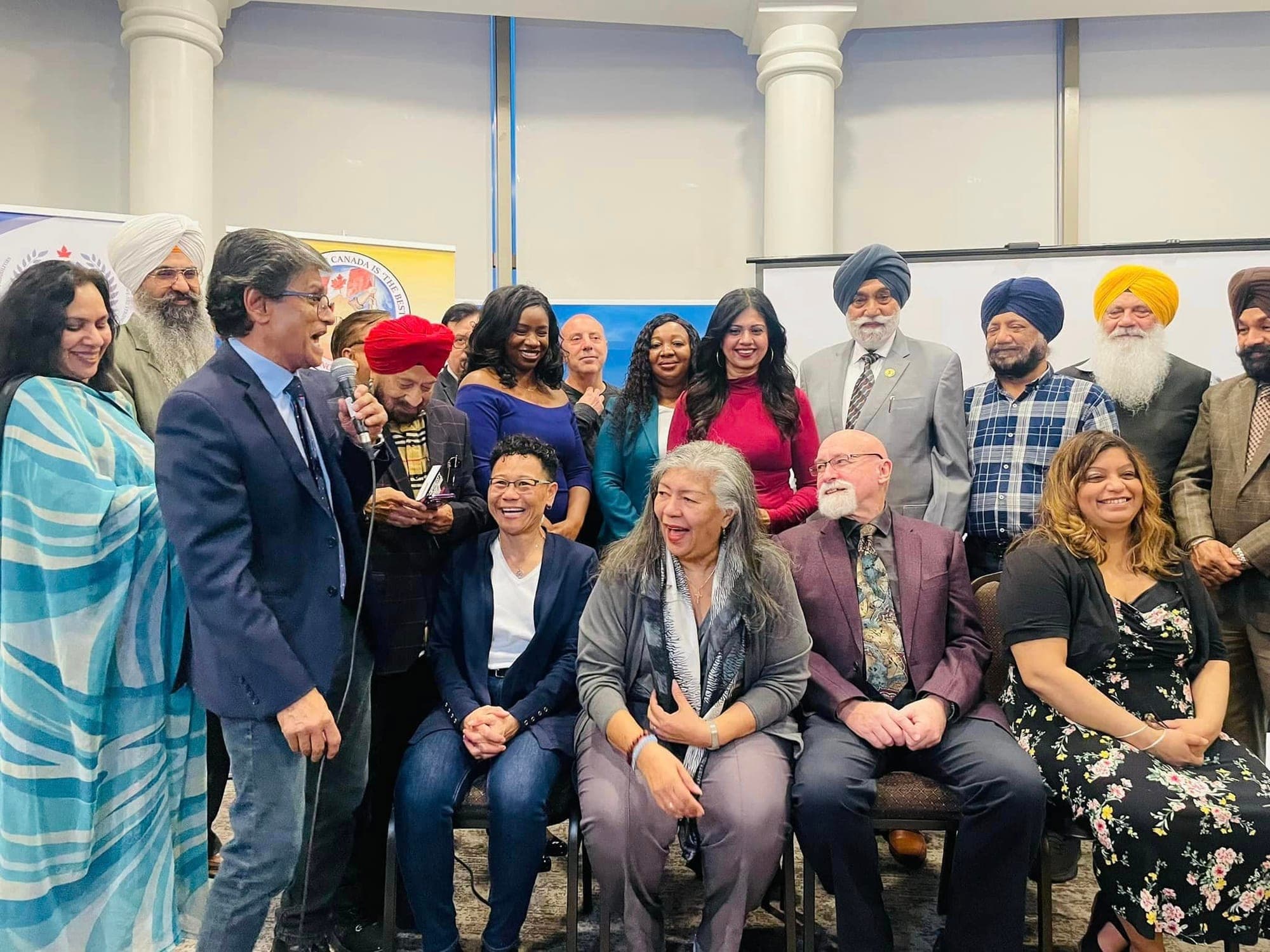 Ehsan Khandaker speaking with a microphone in front of a large group at a community event